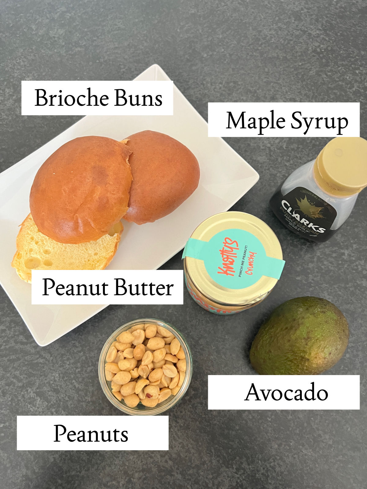 labelled ingredients for peanut butter and avocado toast with white labels and black text on a grey background