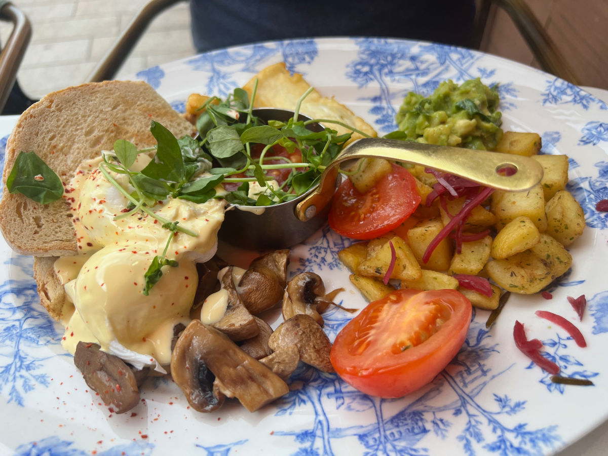 vegetarian english breakfast with hollandaise sauce on a blue and white plate. Salad is served in a small gold pot in the centre.